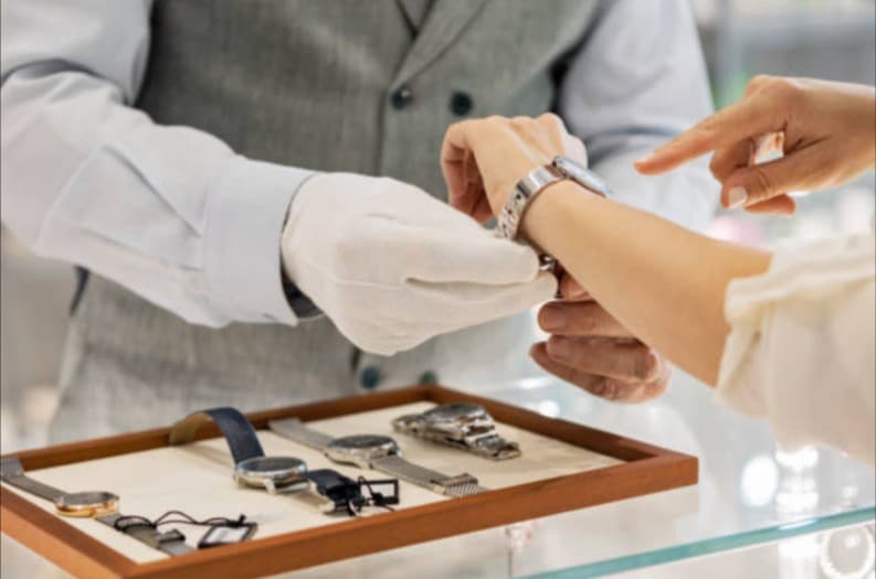 Jewelry store: customer fitting silver watch, watches displayed. Sales and repair.