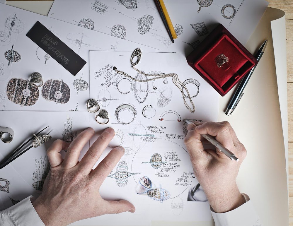 Susie's Jewelry Repair a person drawing on paper with a pen and a ring
